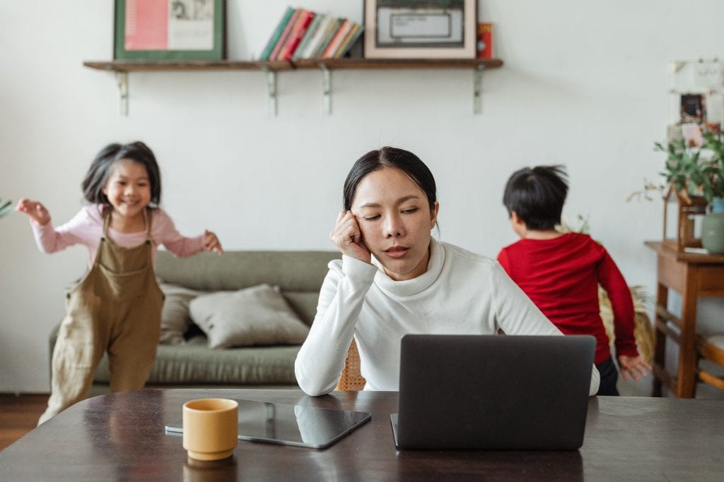 A woman tries to work with children playing behind her