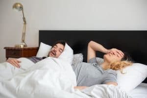 Husband snoring and wife with her hand on her head, tired and frustrated