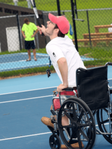 boy in a wheelchair playing tennis vigorously