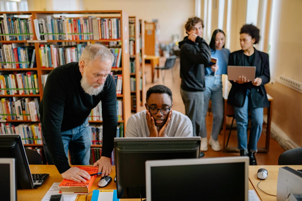 student and teacher in the library reviewing work on a computer