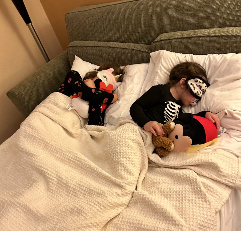 two girls sleeping with light-blocking masks on a sofe bed.
