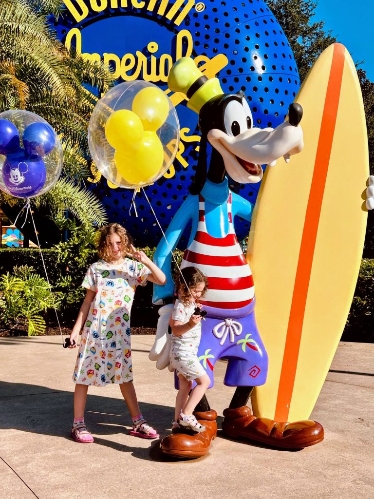 Two little girls with a statue of Goofy surfing