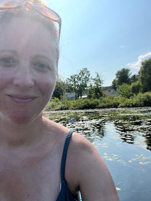 selfie of a smiling woman. she appears to be in a canoe on the water.